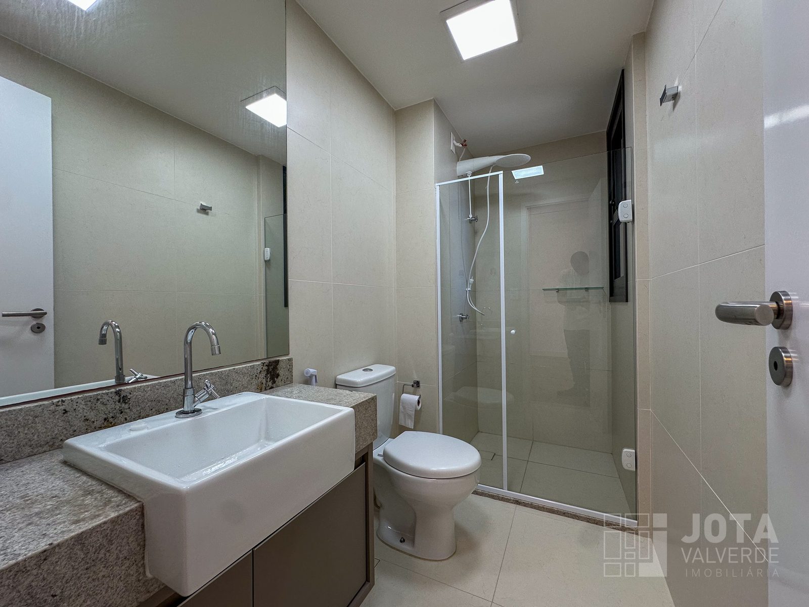 Banheiro social do apartamento, com box de vidro e bancada em granito