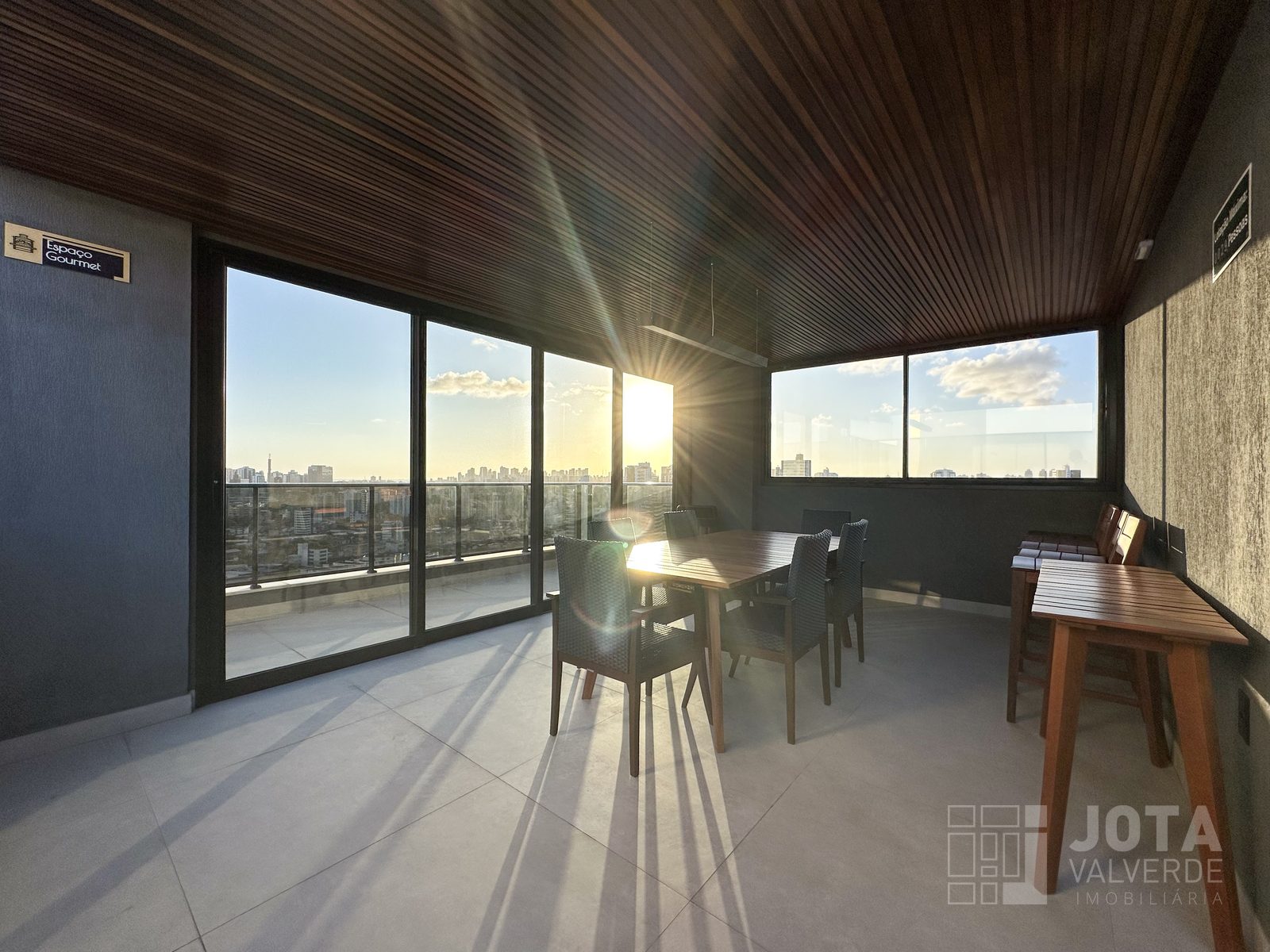 Salão do espaço gourmet com mesa para oito lugares e vista panorâmica ao pôr do sol