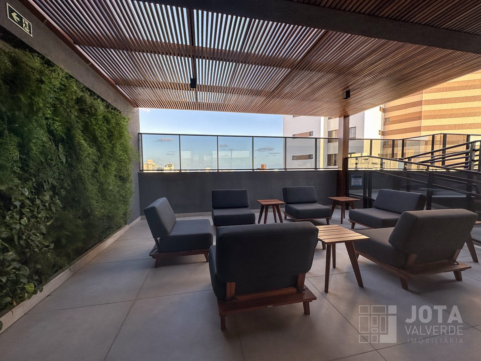 Lounge com jardim vertical, poltronas e mesas de madeira